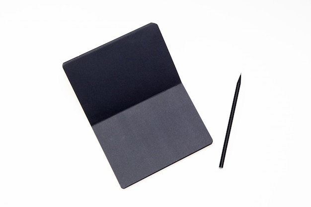 Caderno com papel preto e lápis sobre fundo branco.
