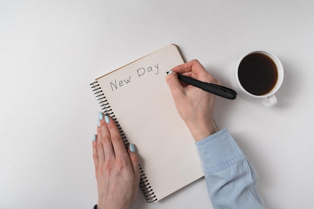 Caderno com texto do novo dia mãos femininas escrevendo no bloco de notas e xícara de café em fundo branco