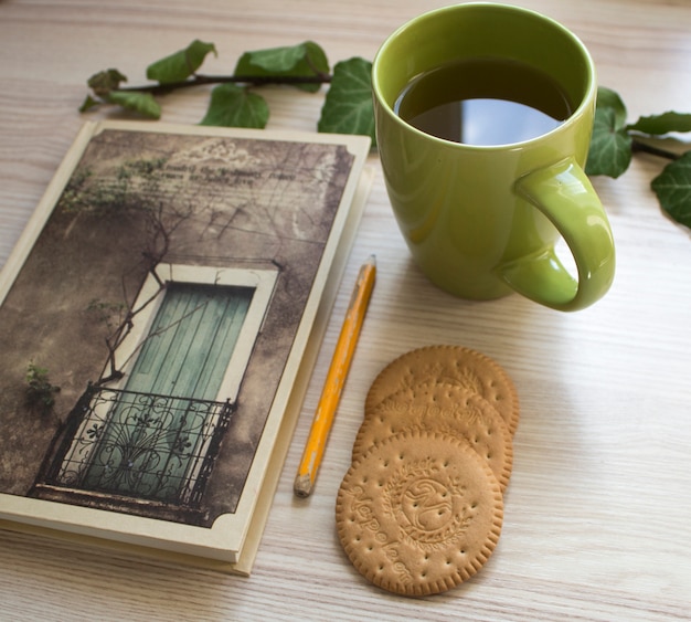 caderno com um lápis, uma xícara de chá, um biscoito e um ramo