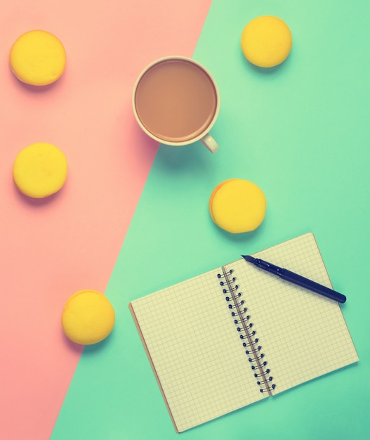 Caderno com uma caneta, uma xícara de café e biscoitos amarelos em um pastel colorido.