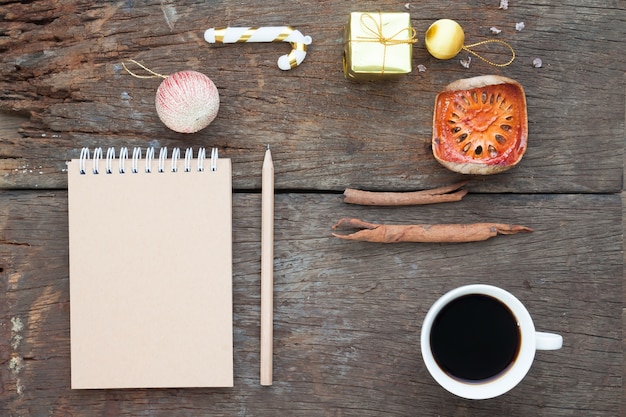 Caderno de artesanato, lápis, xícara de café e enfeites de natal na mesa de madeira antiga, flat lay