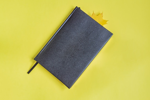 Caderno de couro falso de cor preta com folha de bordo como marcador em amarelo.