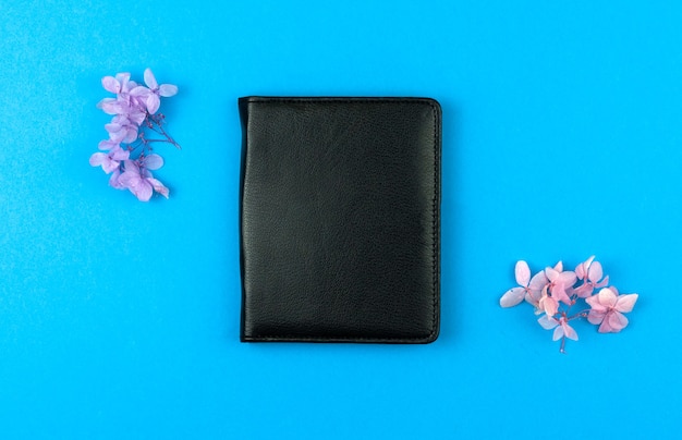 Caderno de couro preto com flores secas em um fundo azul da área de trabalho, configuração plana e foto de vista superior