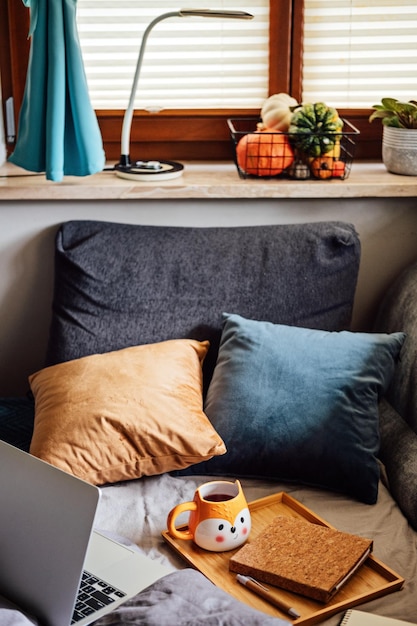 Caderno de laptop quente de outono aconchegante e xícara de chá na bandeja no cobertor na cama no interior