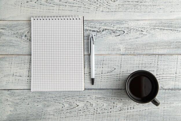 Caderno de papel, caneta e xícara de chá ou café em madeira branca gasto vintage, vista superior