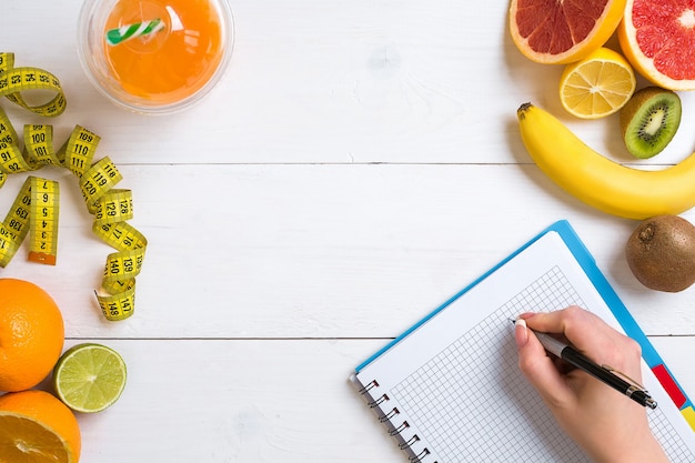 Caderno de suco fresco em copo de frutas cítricas, limão, toranja, laranja com lápis em madeira branca ...