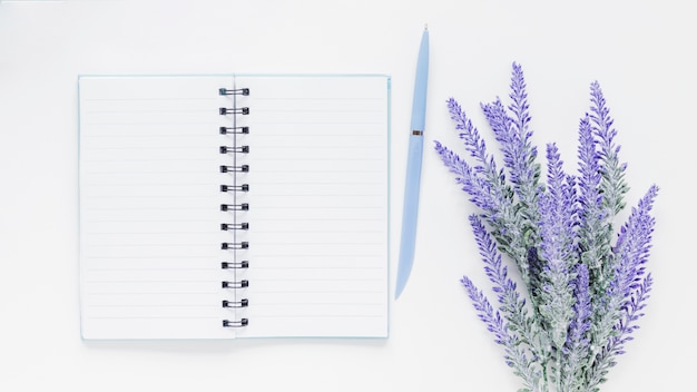 Caderno e caneta perto de flores de lavanda na mesa branca