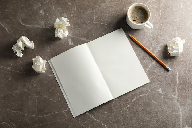 Caderno em branco, bolas de papel, lápis e xícara de café sobre fundo cinza, vista superior