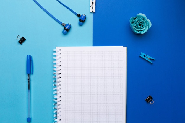 Caderno em branco com caneta e fones de ouvido sobre fundo azul. Espaço livre para texto, anúncio.