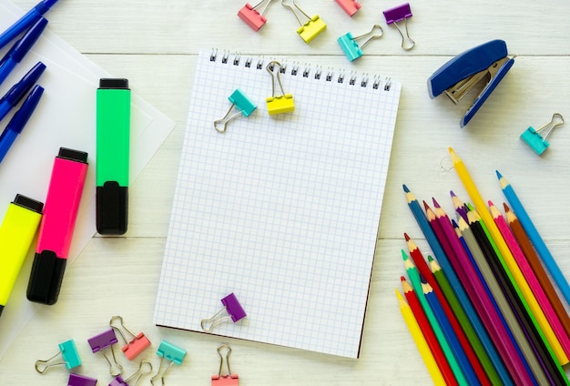 Caderno em branco com vários artigos de papelaria em um fundo branco de madeira