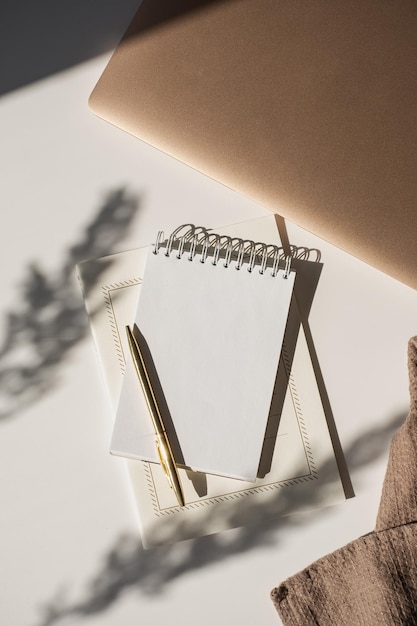 Caderno espiral com espaço para cópia em branco caneta laptop em flores luz solar sombra na mesa branca Espaço de trabalho minimalista boêmio estético Modelo de escritor de artista