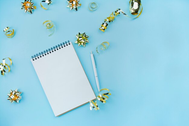 Caderno espiral em branco com caneta branca sobre um fundo azul com confetes e arcos dourados. Cor e estilo na moda. Postura plana. Copie o espaço. Idéia do Blogger.