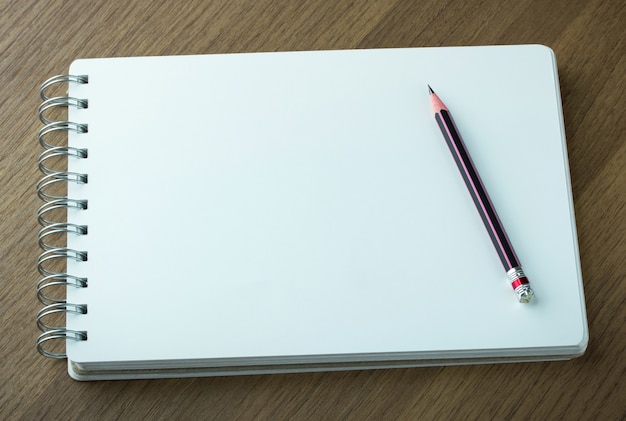 caderno espiral em branco e lápis em fundo de madeira escura