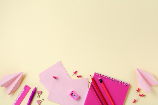 Caderno, lápis de cor, régua, caneta, borracha, apontador e papelaria de escola e escritório em fundo amarelo.