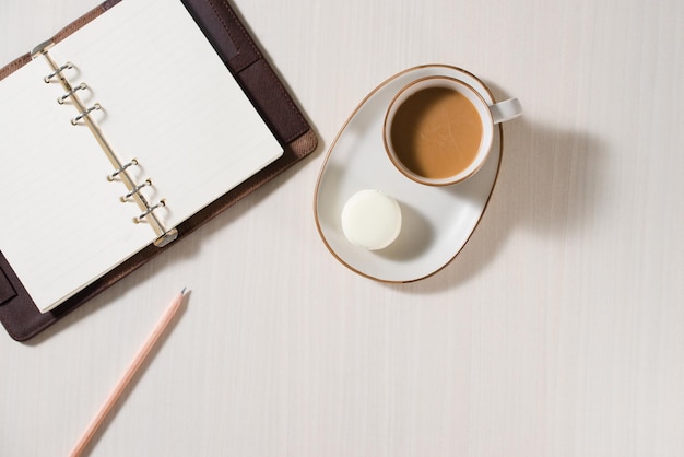 Caderno limpo, xícara de café e macaron colorido na vista superior da mesa cinza. Café da manhã aconchegante. Postura plana de moda. Doces macarons.