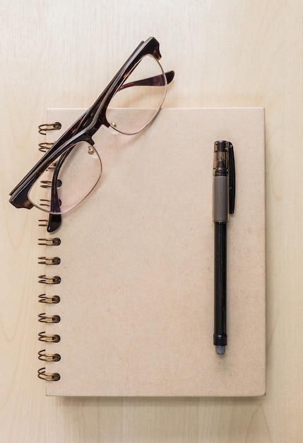 Caderno marrom com óculos e caneta preta sobre fundo de madeira