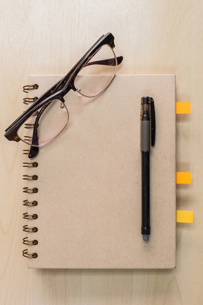 Caderno marrom com óculos e caneta preta sobre fundo de madeira