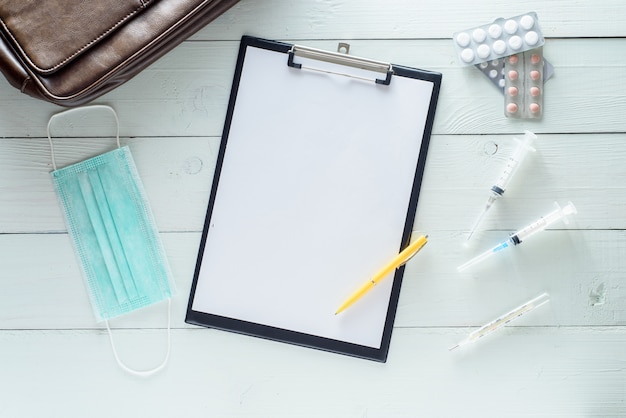 Caderno para anotações, medicamentos, seringas. Filmado em uma mesa de madeira branca de cima.