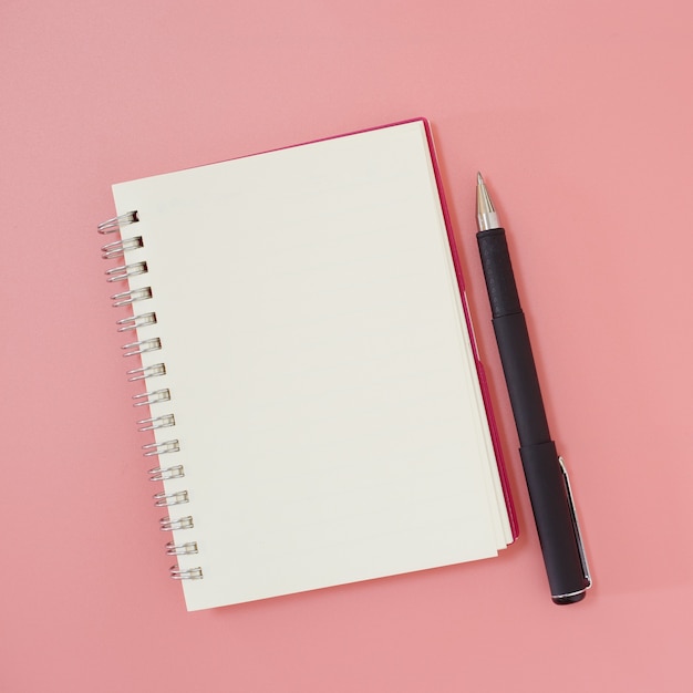 Caderno vazio e caneta para fazer a lista no fundo rosa, espaço de trabalho para vista superior do texto.