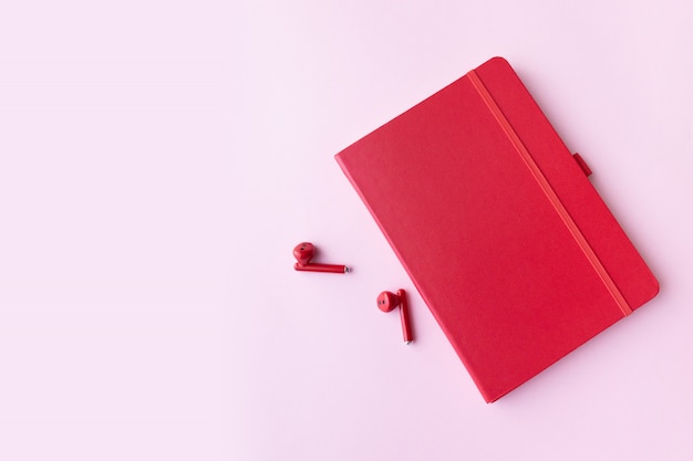 Caderno vermelho com fones de ouvido sem fio na parede rosa com espaço de cópia. Conceito mínimo de negócios