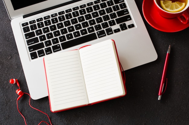 Foto caderno vermelho em branco, computador portátil, fones de ouvido e xícara de chá.