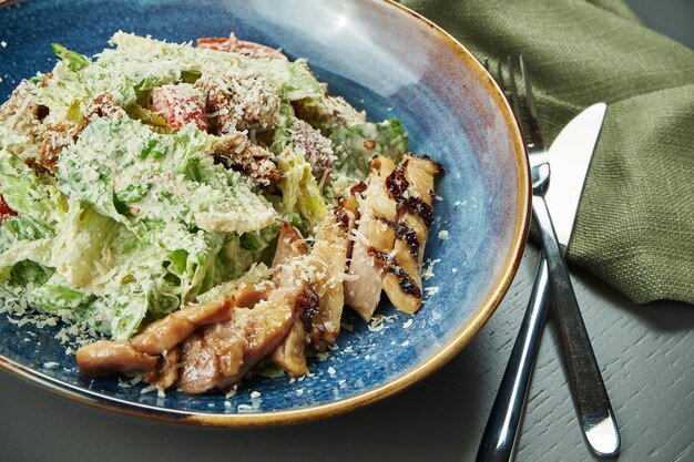 Caesar Salat mit Croutons, Parmesan, Huhn, Ei in blauer Schüssel auf Holztisch. Restaurant servieren. Nahaufnahme, selektiver Fokus