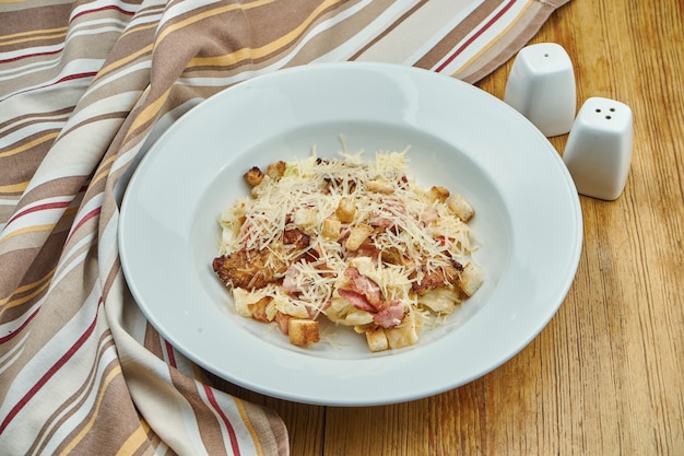 Caesar Salat mit Croutons, Parmesan, Speck, Huhn, Ei in Whte Bowl auf weißer Oberfläche. Restaurant servieren. Schließen Sie mit Kopierraum.