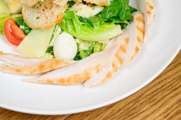 Caesar Salat mit Croutons, Wachteleiern, Kirschtomaten und gegrilltem Hähnchen in Holztisch. Köstlicher Salat mit Hähnchen, Nüssen, Ei und Gemüse.