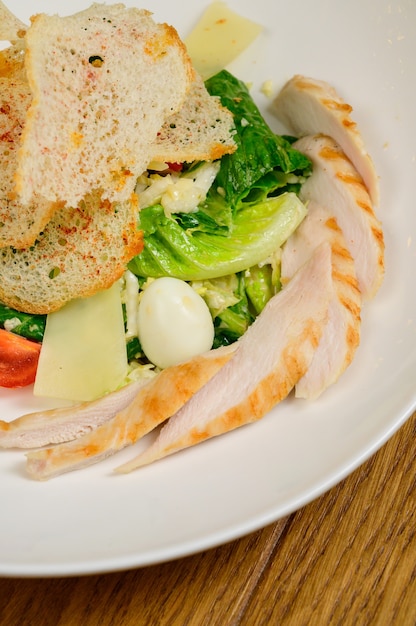 Caesar salat mit croutons, wachteleiern, kirschtomaten und gegrilltem hähnchen in holztisch. köstlicher salat mit hähnchen, nüssen, ei und gemüse.