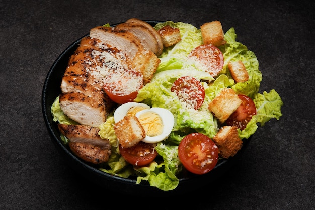 Caesar-Salat mit Hähnchenbrust, Kirschtomaten und Parmesan auf dunklem Hintergrund, Nahaufnahme