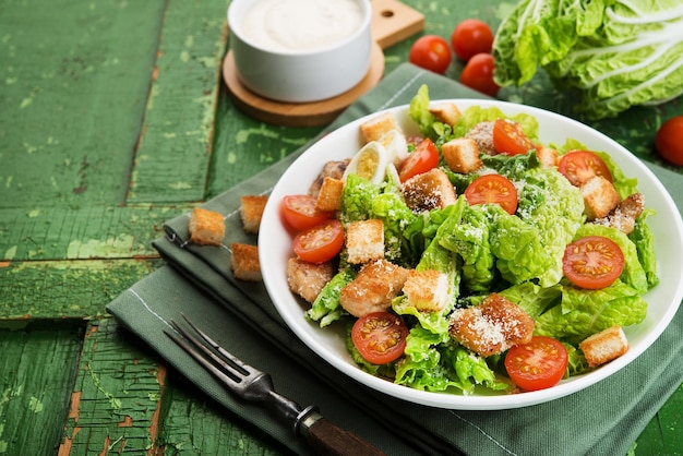 Caesar-Salat mit Hähnchenfilet, Tomaten, Croutons und Parmesan in einem Teller auf rustikalem Holzhintergrund, Kopierraum