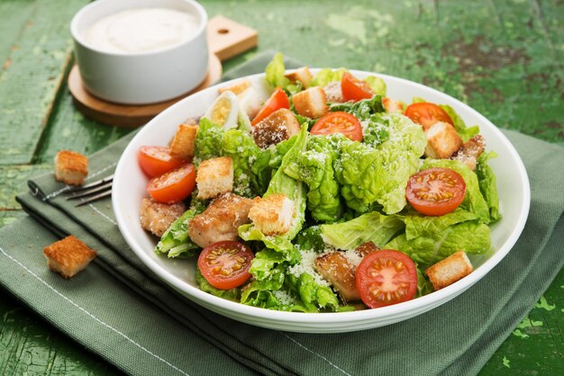 Caesar-Salat mit Hähnchenfilet, Tomaten, Croutons und Parmesan in einem Teller auf rustikalem Holzhintergrund, Nahaufnahme