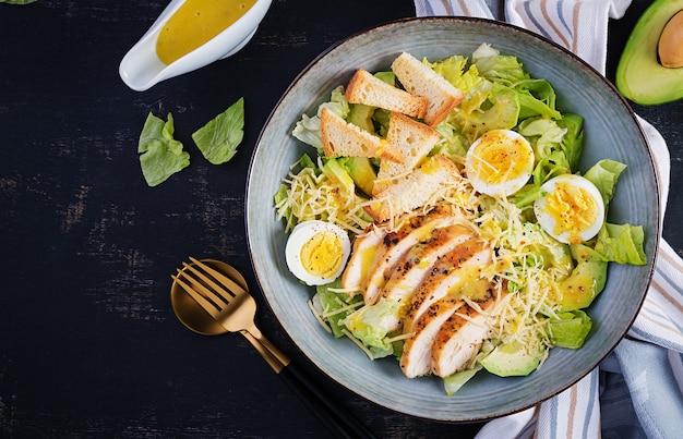 Caesar-Salat mit Salat, Hühnchen, Avocado und Croutons auf dunklem Tisch