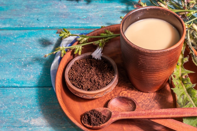 Café de achicoria natural con flores frescas y polvo. Bebida sin cafeína en vaso de cerámica. Reemplazo alternativo del café, cafeína. Fondo de madera turquesa, lugar para texto