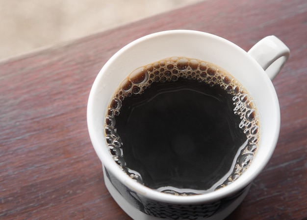 Café americano quente em uma caneca sobre uma tábua de madeira servido no café da manhã.