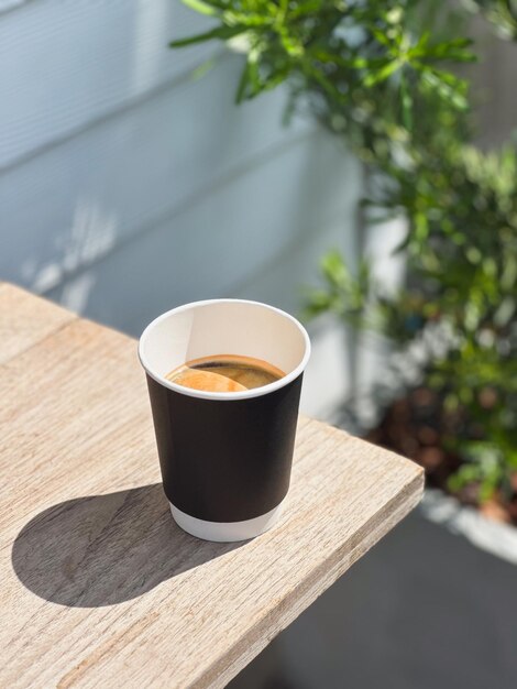 Café americano en taza de papel en una mesa de madera
