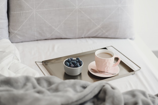 Café y arándanos en una bandeja de metal servido en una cama. Desayuno ligero por la mañana.