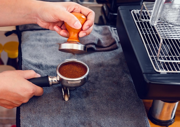 Café barista fazendo café com prensas manuais de café moído usando tamper na barra de balcão de madeira