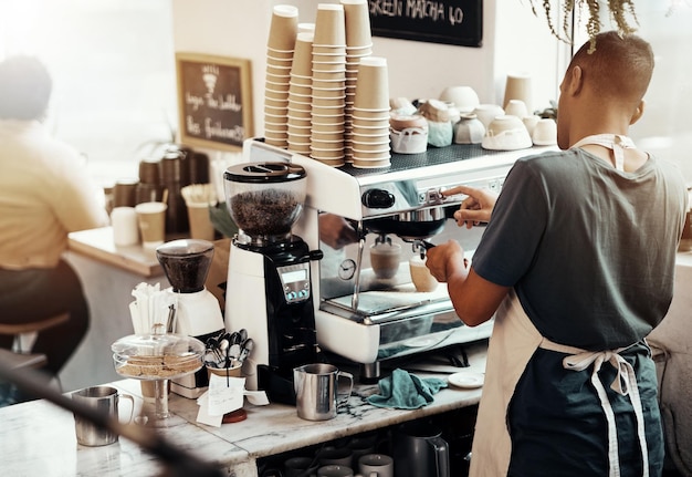 Café barista hombre y servidor en la máquina de café para preparar café expreso o capuchino Vista posterior mesero y trabajador de la cafetería vertiendo cafeína en el servicio de hospitalidad del restaurante y orden de bebidas