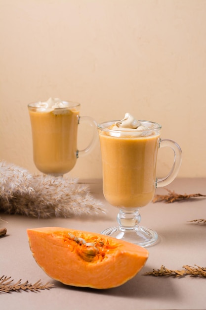 Café batido de calabaza con canela en vasos y una rodaja de calabaza sobre un fondo beige. Bebidas caseras calientes de otoño. Vista vertical