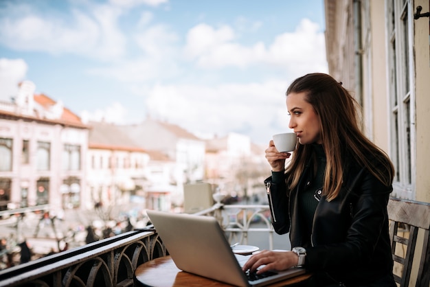 Café bebendo da mulher no wihle do terraço que trabalha em um portátil.