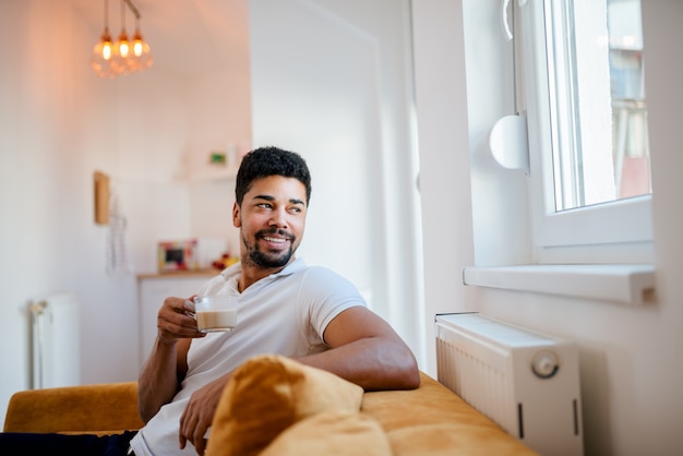 Café bebendo do homem afro-americano considerável e vista através da janela em casa.