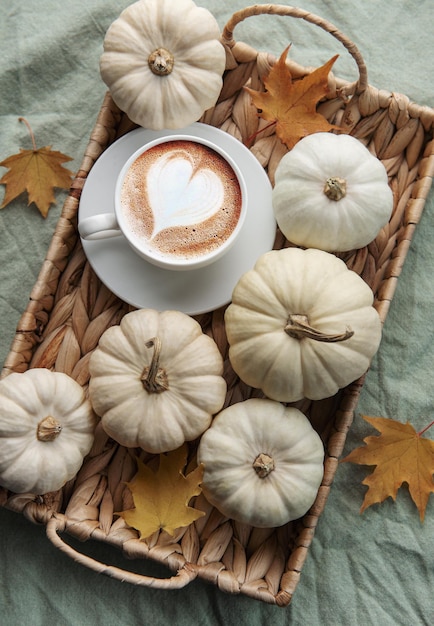Café de calabazas blancas y hojas de otoño en una bandeja de mimbre