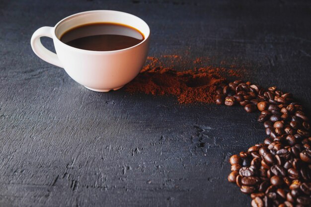 Café caliente con café en polvo y granos de café sobre un fondo negro