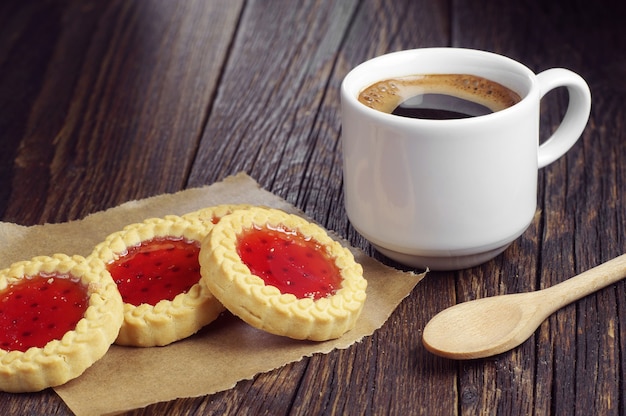 Café caliente y galletas con mermelada en la mesa de madera oscura.