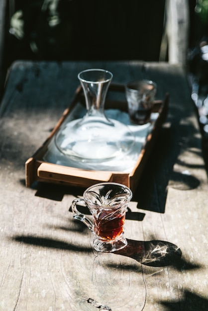 Café caliente del goteo en vidrio de consumición en la tabla de madera con luz del sol dura.