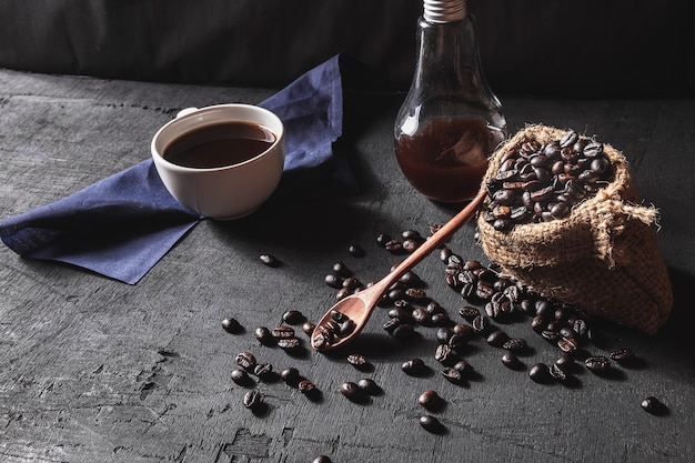 Café caliente y granos de café crudos en un fondo negro.