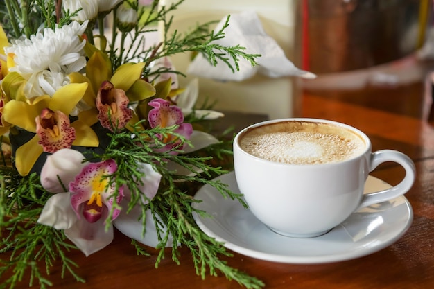 Café caliente, listo para beber en una taza de café, colocado junto a un florero