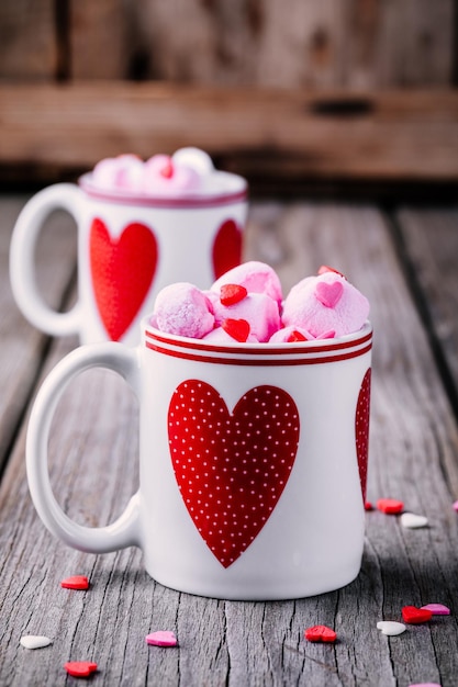 Café caliente con malvaviscos rosas en tazas con corazones sobre un fondo de madera para el día de San Valentín