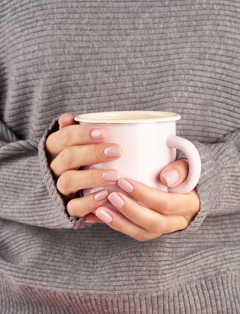 Café caliente de la mañana en el trabajo en una fría mañana de otoño, manos sosteniendo una taza con una bebida, suéter gris